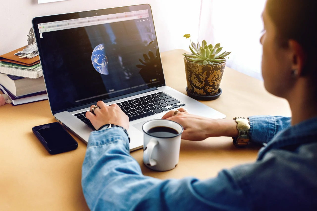 Girl with coffee on background of laptop map and succulent in morning light.