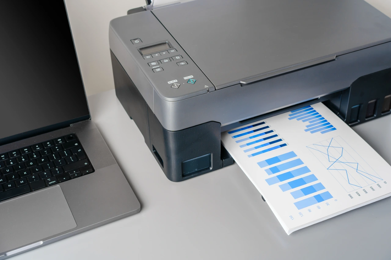 Printer and laptop on grey table in office